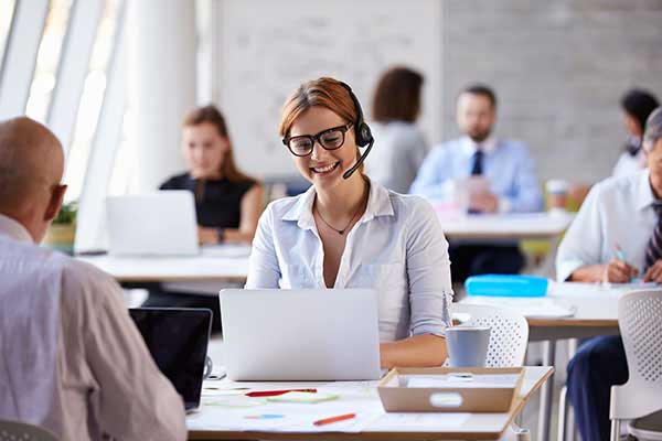 Female customs clearance officer with full framed specs, talking through a headset by using a laptop